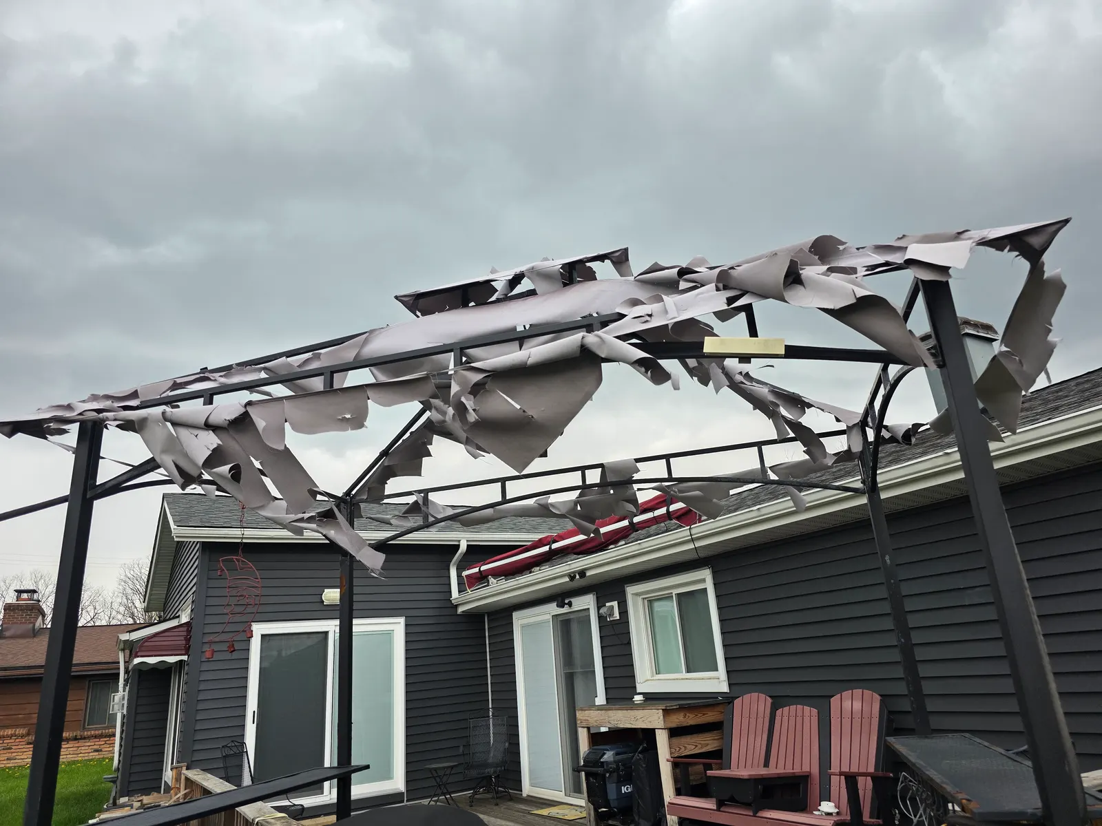 Metal patio cover torn apart by a hail and wind storm behind a gray house